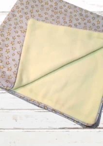 manta de bebê dobrada, um lado em cinza com estampa de estrelinhas amarelas e um lado em soft amarelo